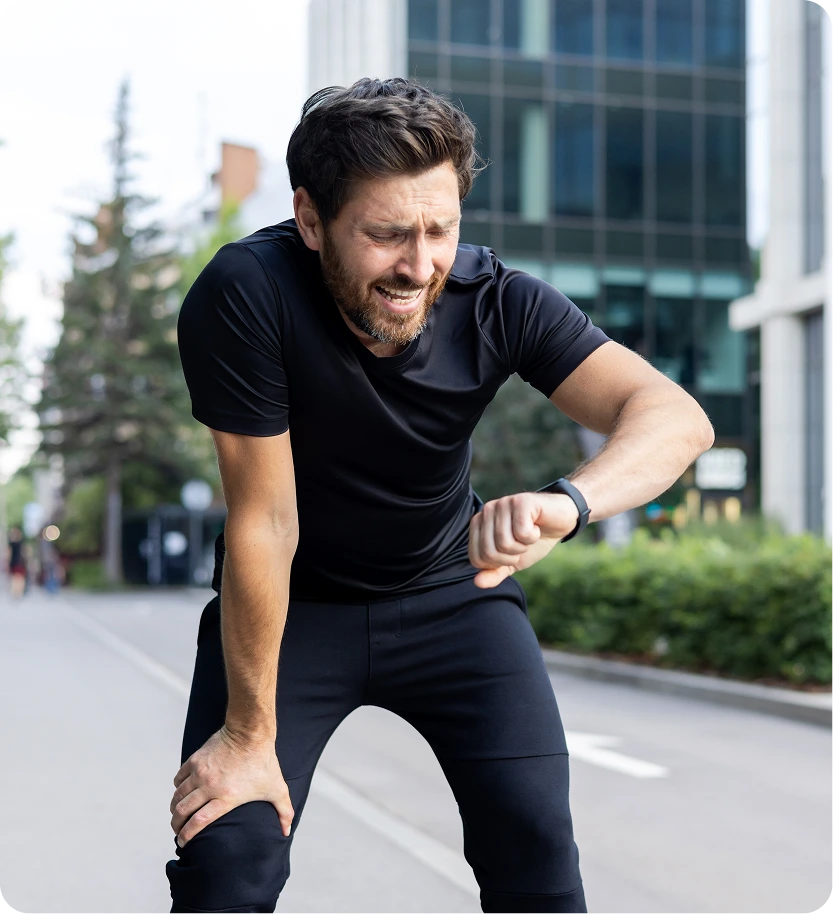 Man in black athletic wear jogging outdoors in an urban setting, checking his smartwatch