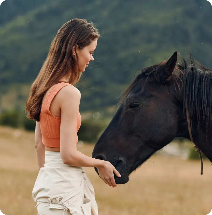 Woman petting a black horse's nose in a mountain valley setting