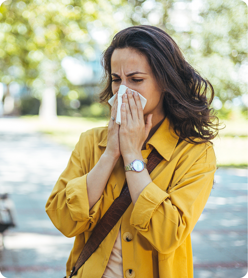 Woman in yellow jacket sneezing into a tissue while outdoors