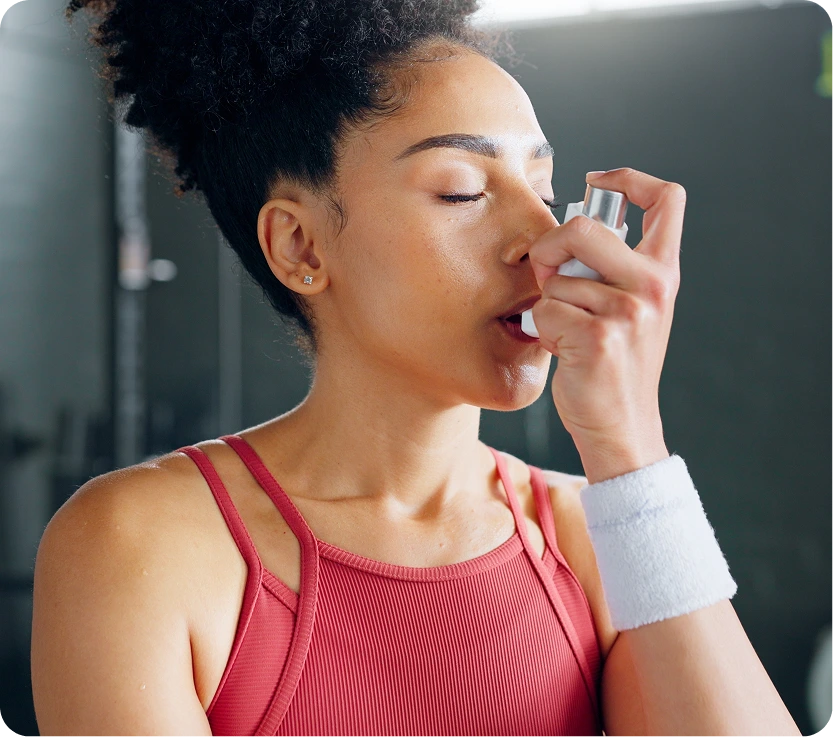 Athlete in pink sports top using an inhaler during exercise