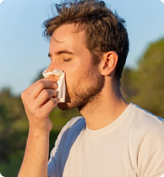 Man blowing his nose into a tissue outdoors
