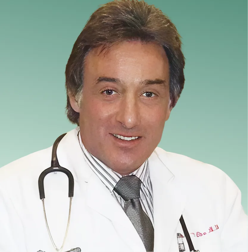 Male physician in white coat and stethoscope smiling against a teal background