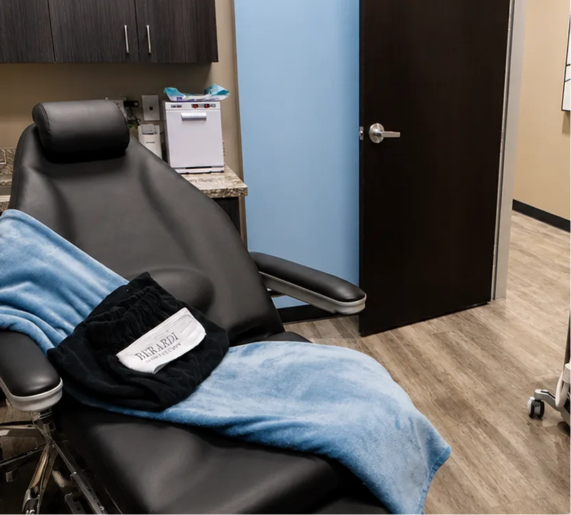Medical exam room with black treatment chair, blue partition, and sterilization equipment