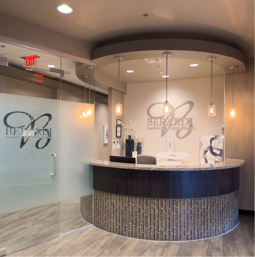 Berardi Aesthetics & Plastic Surgery reception area with curved desk, pendant lighting, and logo on frosted glass entry door