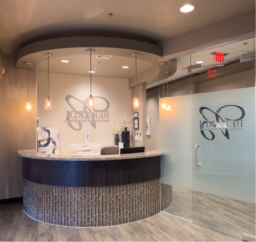 Modern aesthetic practice reception desk with curved black and silver design, pendant lighting, and glass door entrance