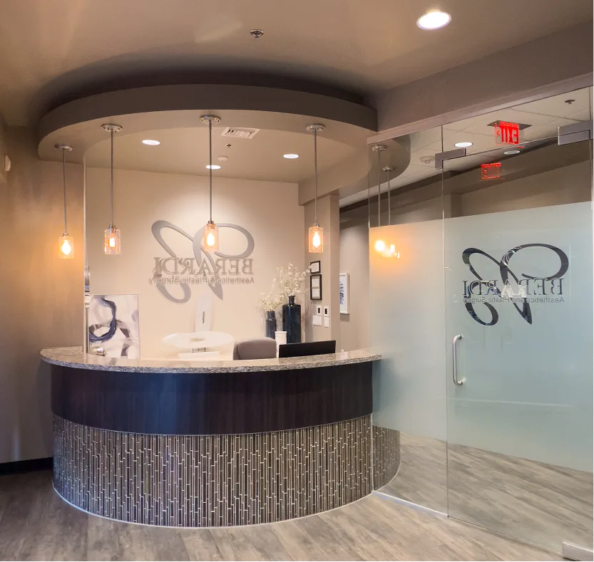 Modern plastic surgery reception desk with curved counter, pendant lighting, and frosted glass door with practice logo