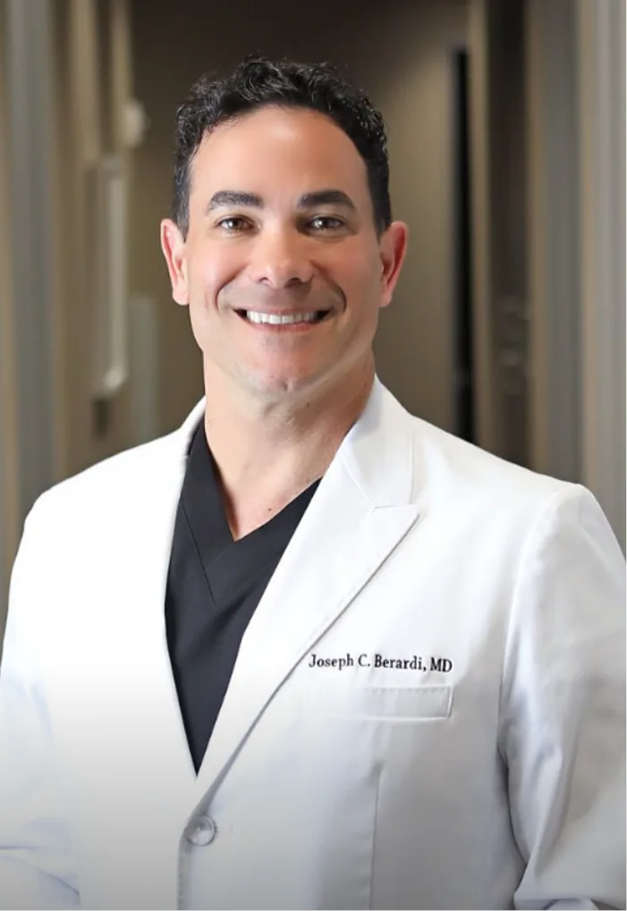 Joseph C. Berardi, MD in white coat over black shirt, smiling at camera in clinical setting