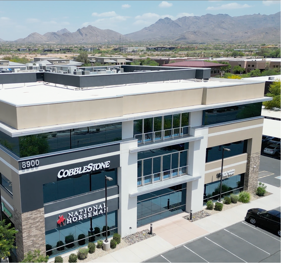 Modern multi-story medical building with CobbleStone and National Horseman signage, mountains visible in background