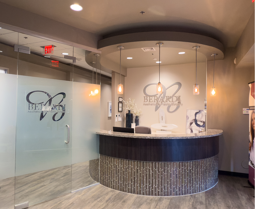 Berardi Aesthetics & Plastic Surgery reception desk with curved counter, pendant lighting, and frosted glass entry door
