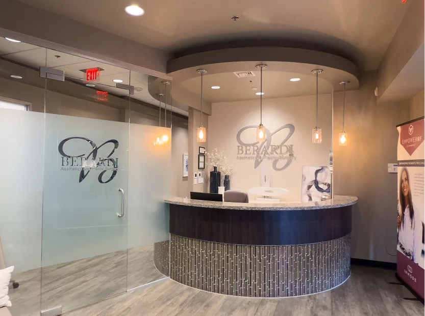 Modern surgical practice reception area with curved desk, pendant lighting, and frosted glass partition with practice logo
