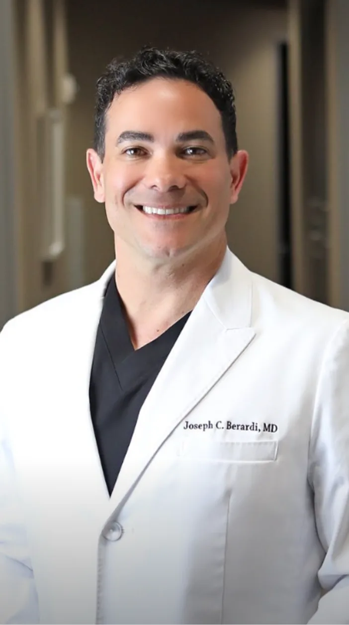 Joseph Berardi, MD, plastic surgeon, smiling in white coat and black shirt