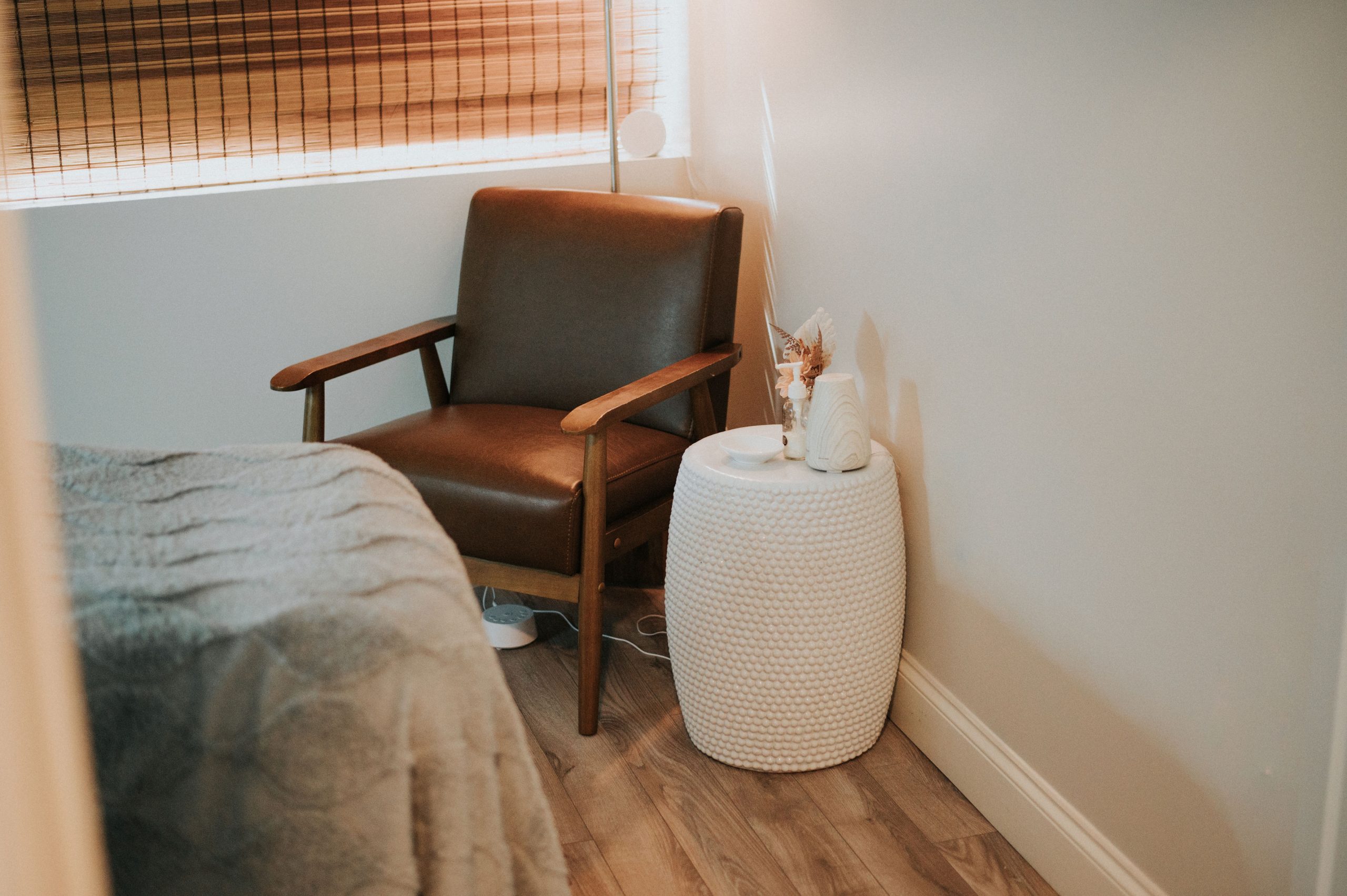 Spa treatment room with leather chair, bed, and white side table with dried flowers