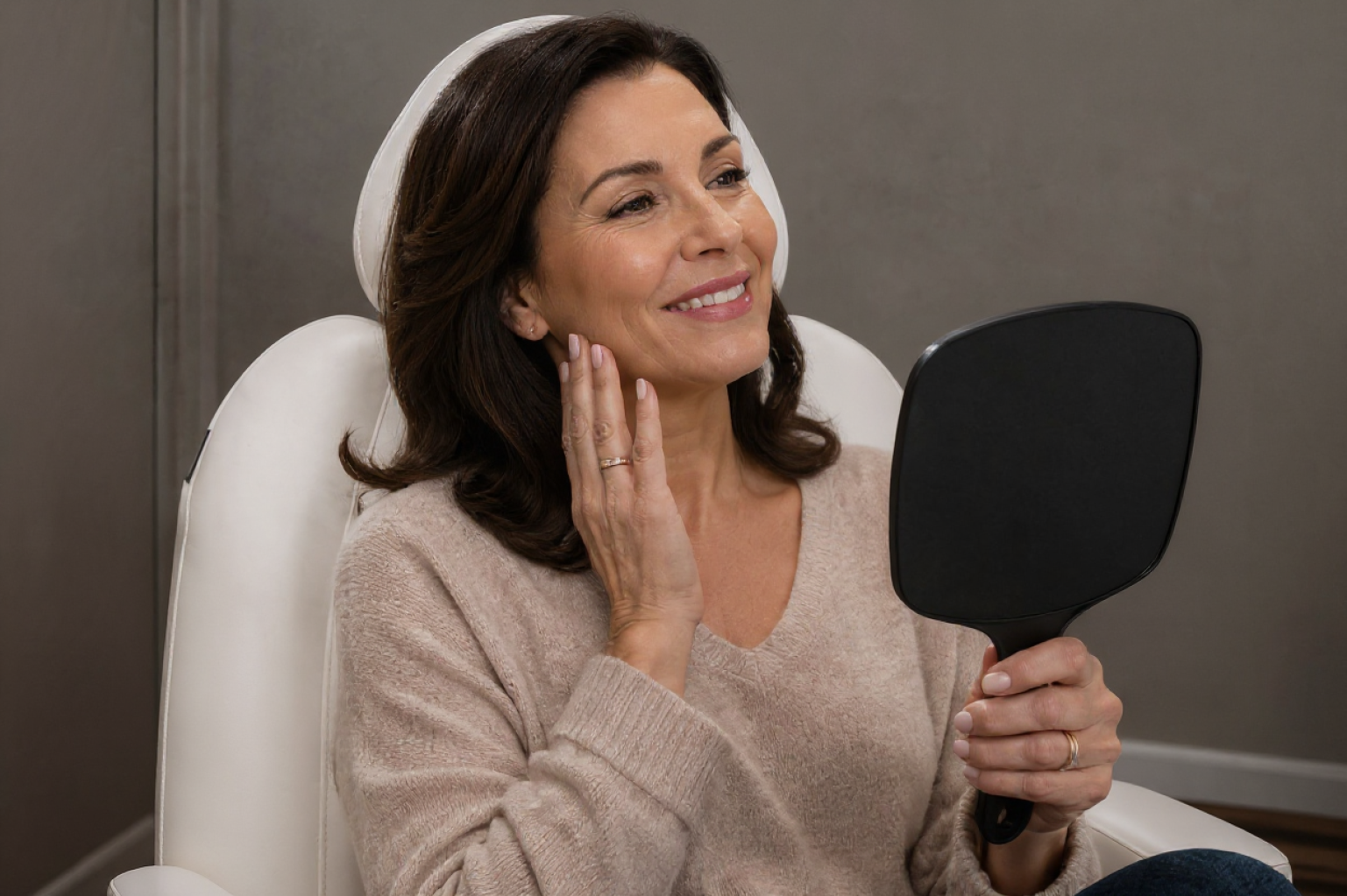 Woman smiling while looking in a handheld mirror after treatment