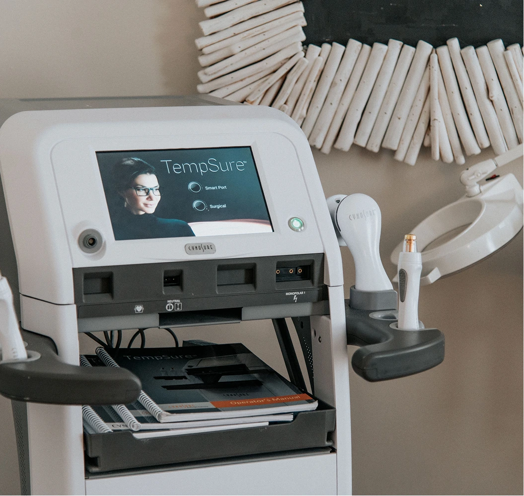 TempSure radiofrequency device with touchscreen display showing treatment modes, handheld applicator, and instruction materials in a clinical setting