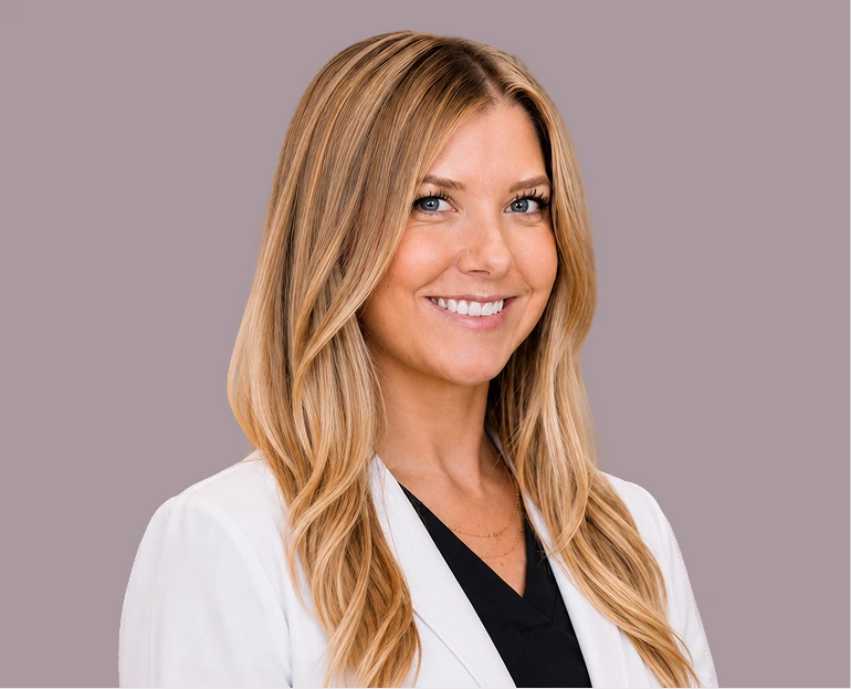 Woman with blonde wavy hair wearing a white coat and black top, smiling at camera