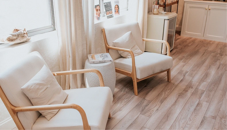 Spa consultation room with cream upholstered chairs, side tables, window, and product shelving