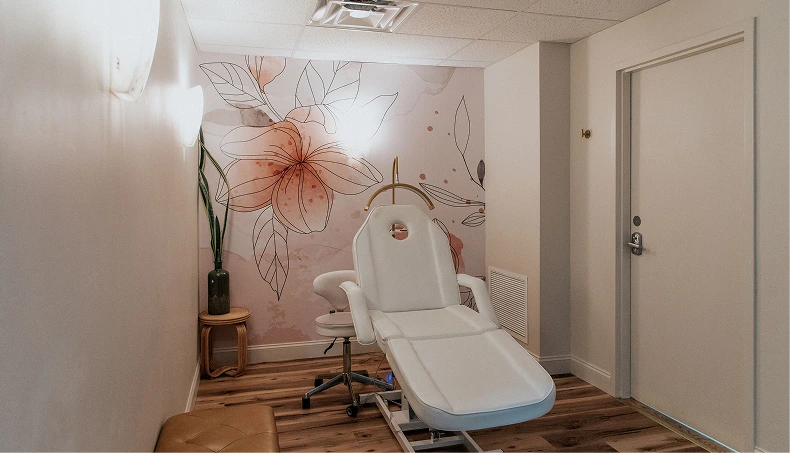 Aesthetic treatment room with white facial bed, orange floral wall mural, and decorative vase