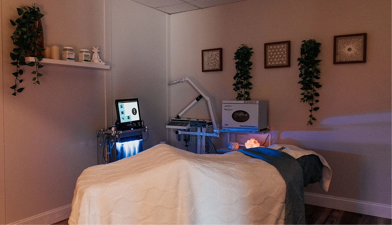 Treatment room with massage bed, computer monitor, blue LED light therapy device, and wall art