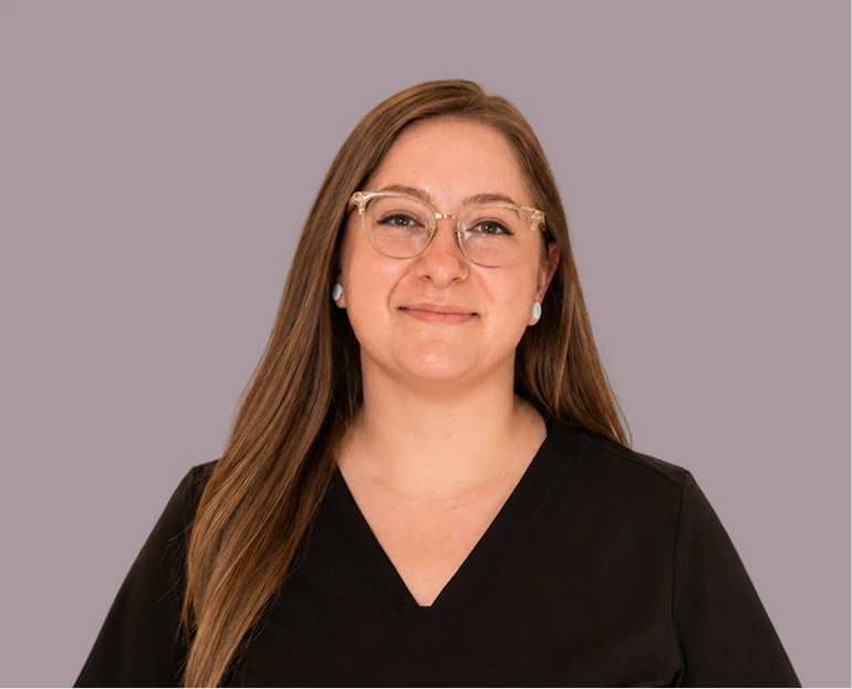 Woman with long brown hair wearing clear-framed glasses and black v-neck against purple background