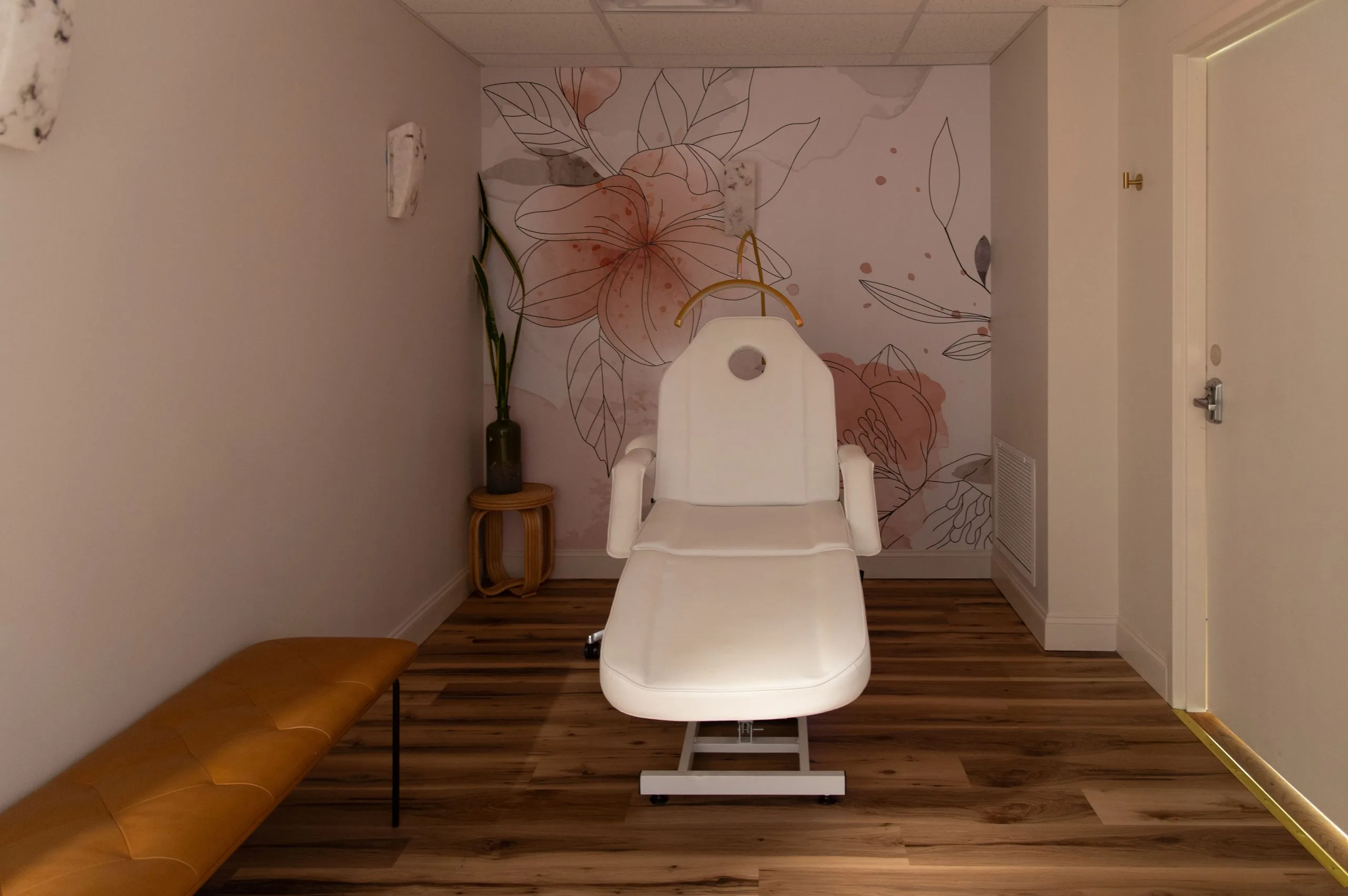 White facial treatment chair in a spa room with floral wall mural and wood flooring