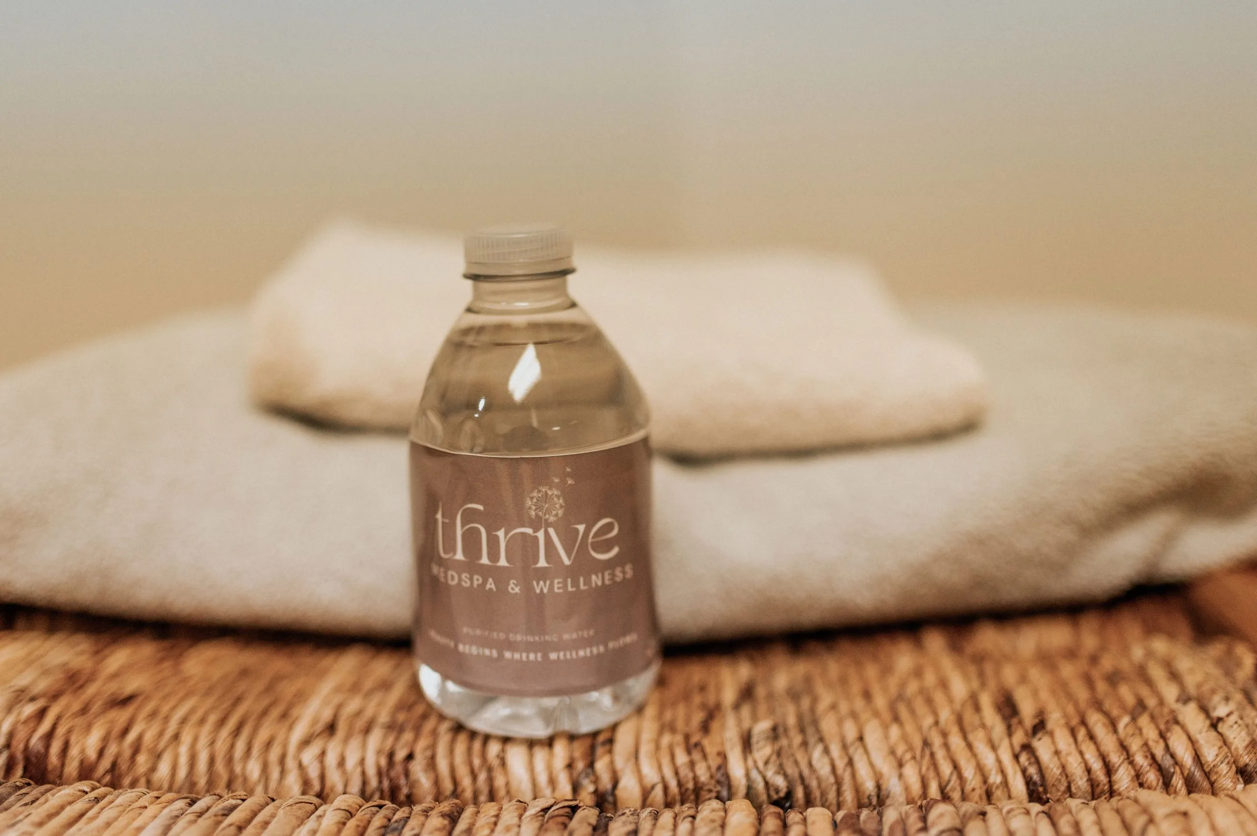 Thrive Med Spa & Wellness branded water bottle on woven mat with rolled towels