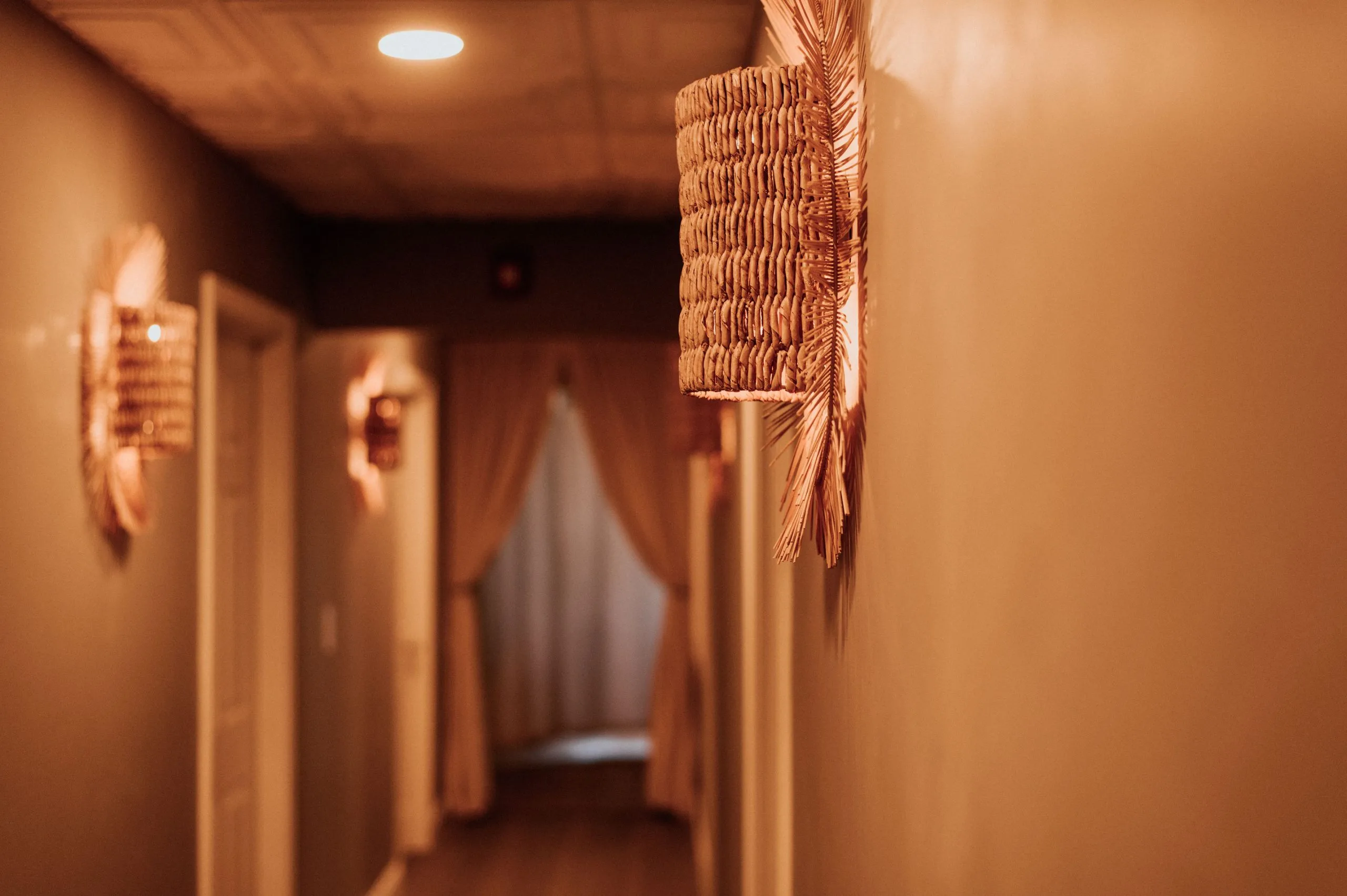 Warm-lit hallway at Thrive Med Spa with woven pendant light and treatment room doorways