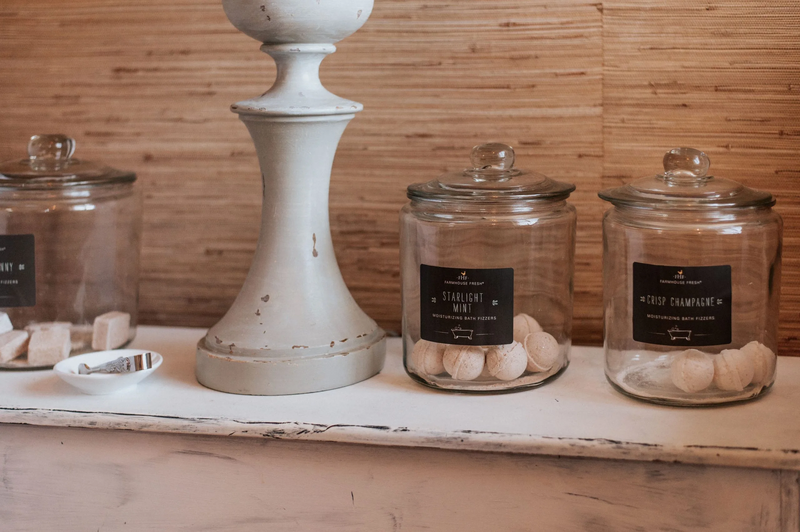 Display of Farmhouse Fresh bath fizzer products including Starlight Mint and Crisp Champagne on wooden shelf with white candlestick