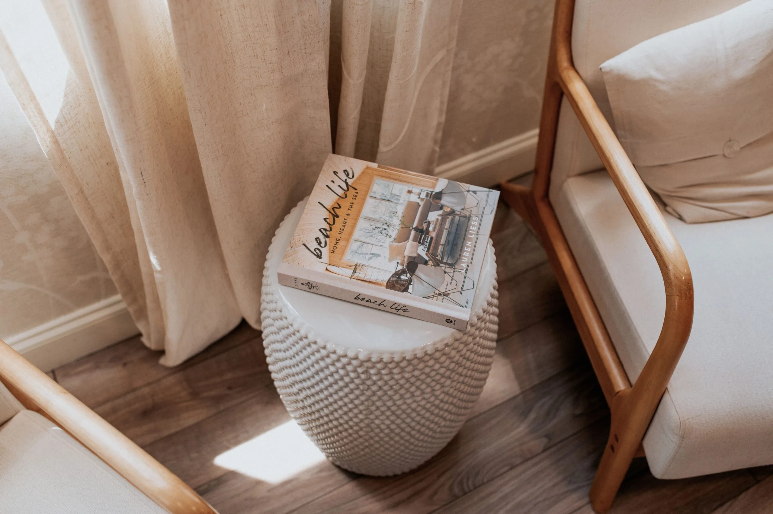 Coffee table books stacked on a woven white side table between two upholstered chairs in a spa waiting room