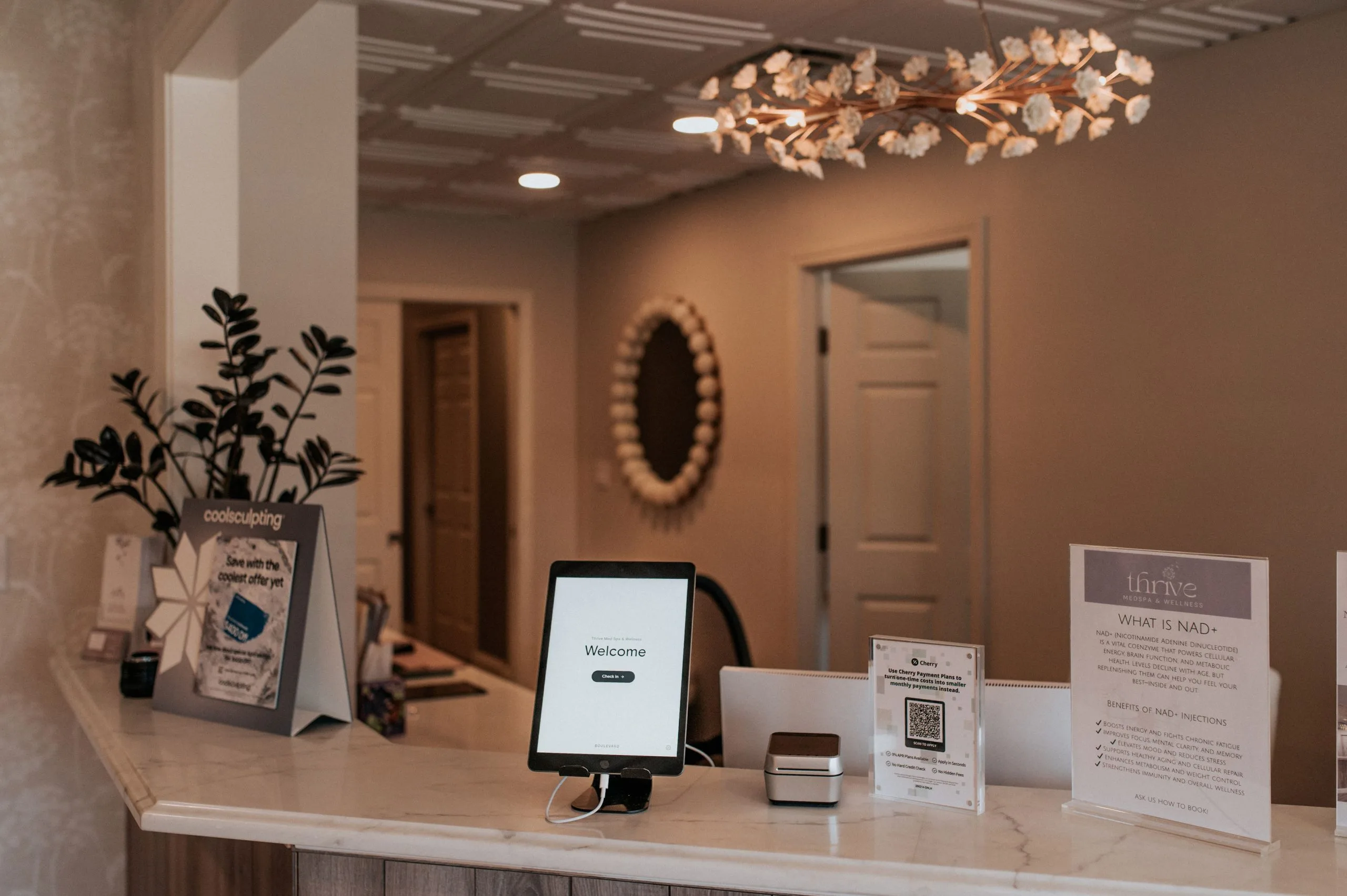 Thrive Med Spa + Wellness reception desk with welcome tablet, informational cards about NAD+ injections, and decorative plants and lighting
