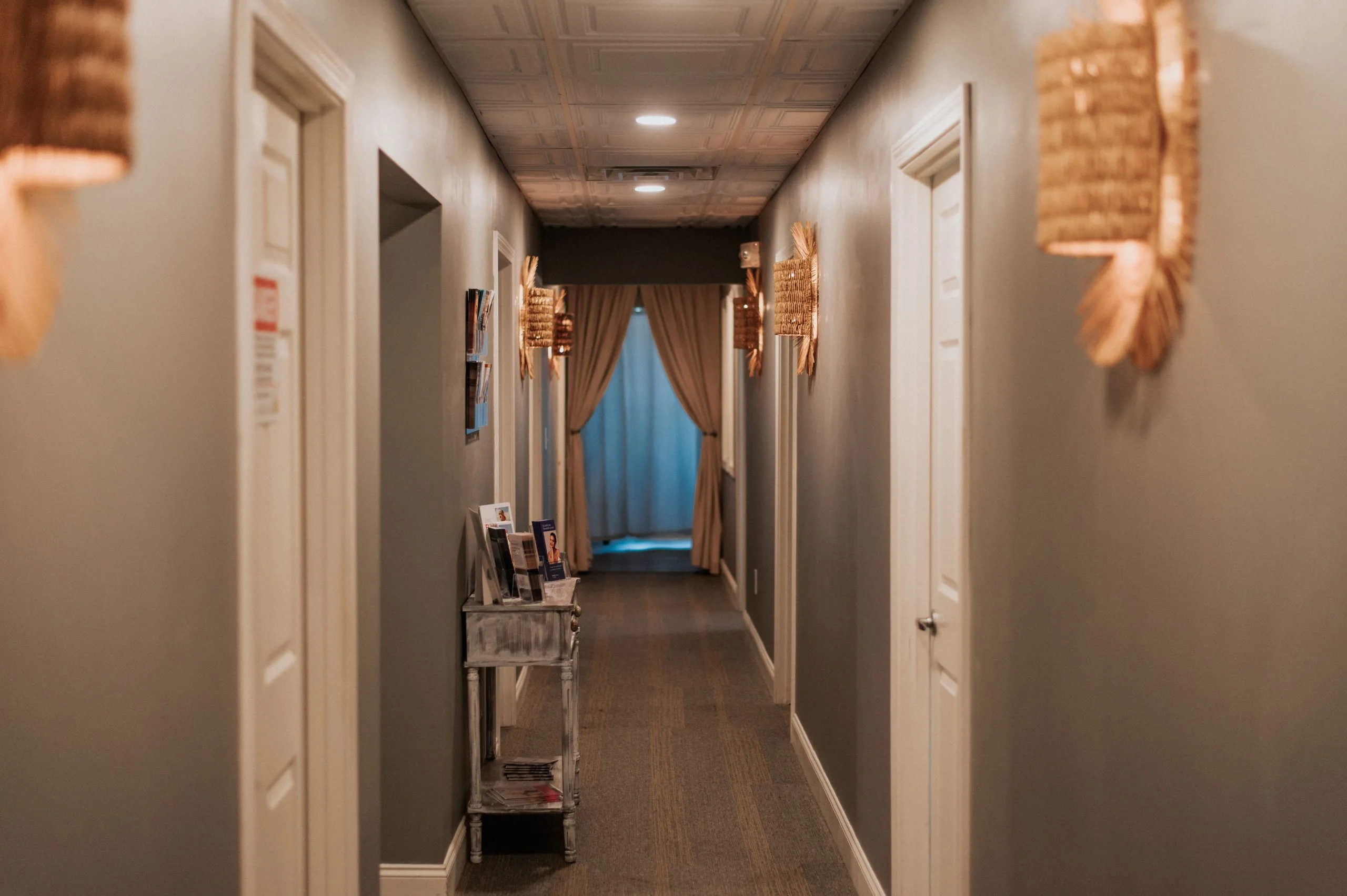 Hallway at Thrive Med Spa with treatment room doors, warm lighting, and calming blue curtains at the end