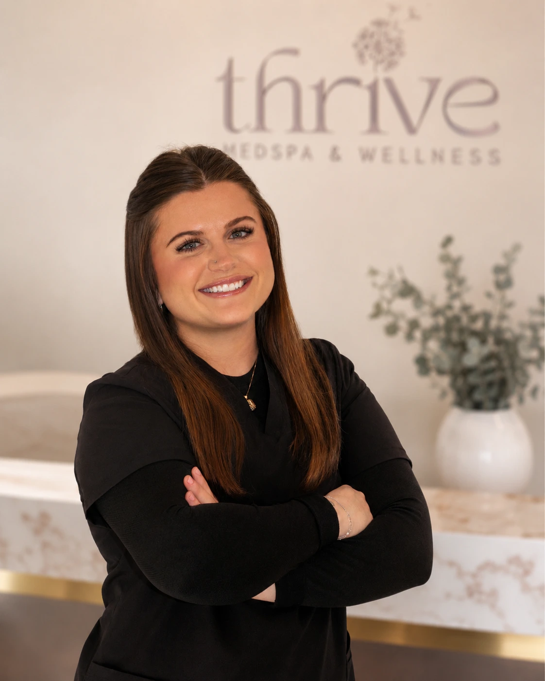 Emily Arsenault, provider at Thrive Med Spa + Wellness, smiling with arms crossed in front of the practice logo
