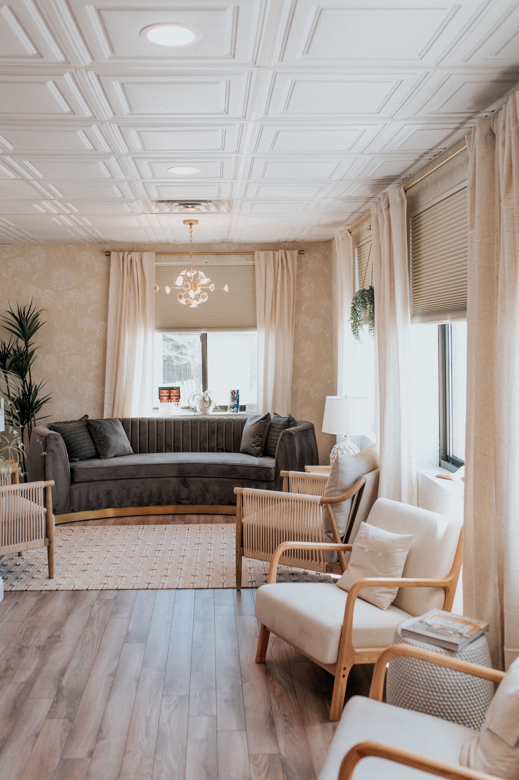 Thrive Med Spa's welcoming consultation room with cream-colored walls, coffered ceiling, gray curved sofa, and natural wood chairs