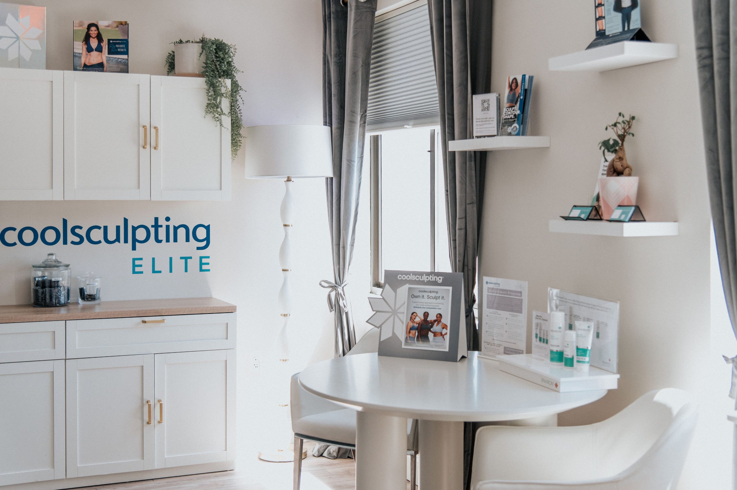 Coolsculpting Elite consultation room with white cabinetry, branded signage, treatment information displays, and a round white table at Thrive Med Spa Portsmouth