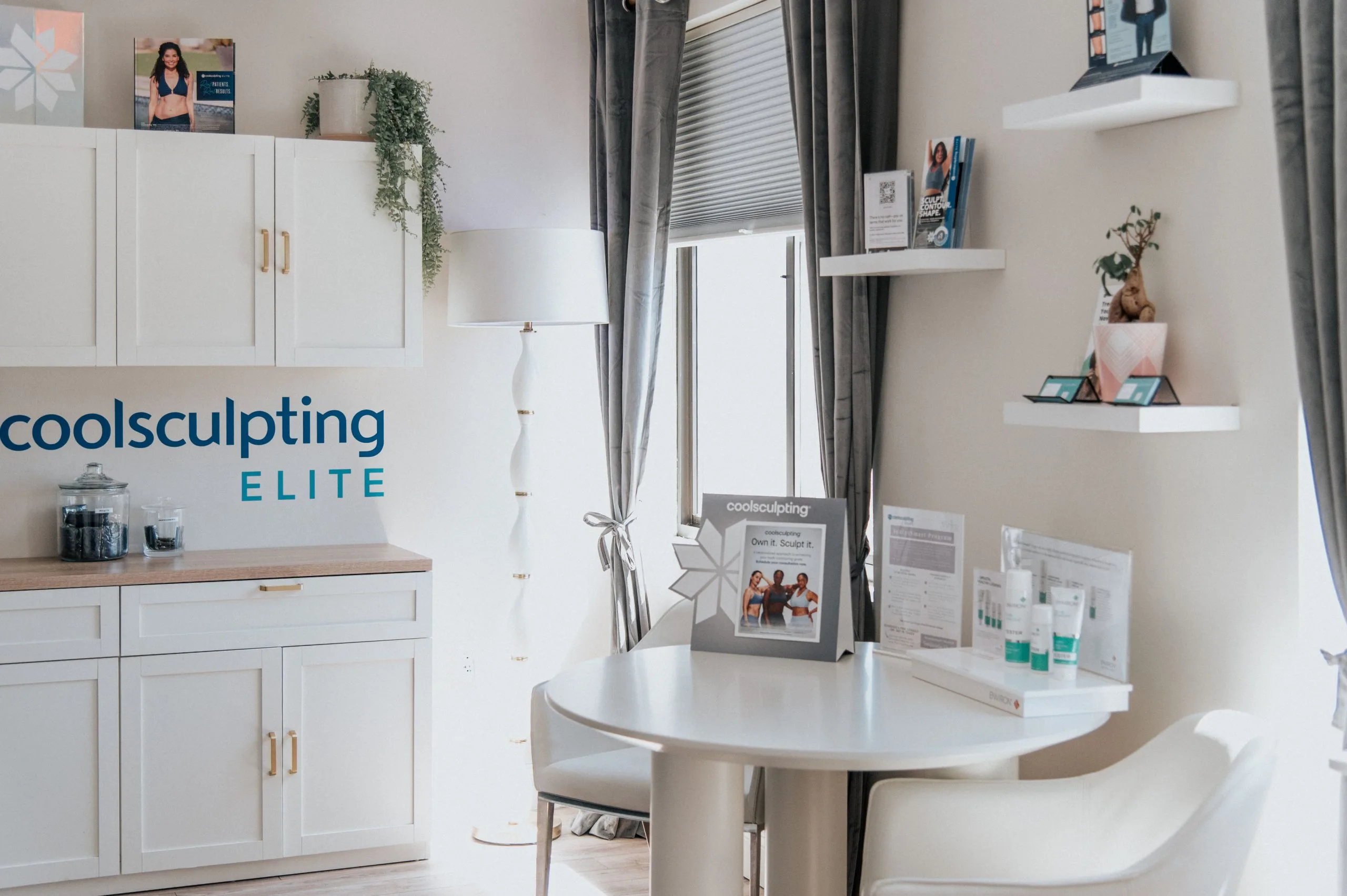 Coolsculpting Elite consultation room with white cabinetry, branded signage, treatment information displays, and a round white table at Thrive Med Spa Portsmouth