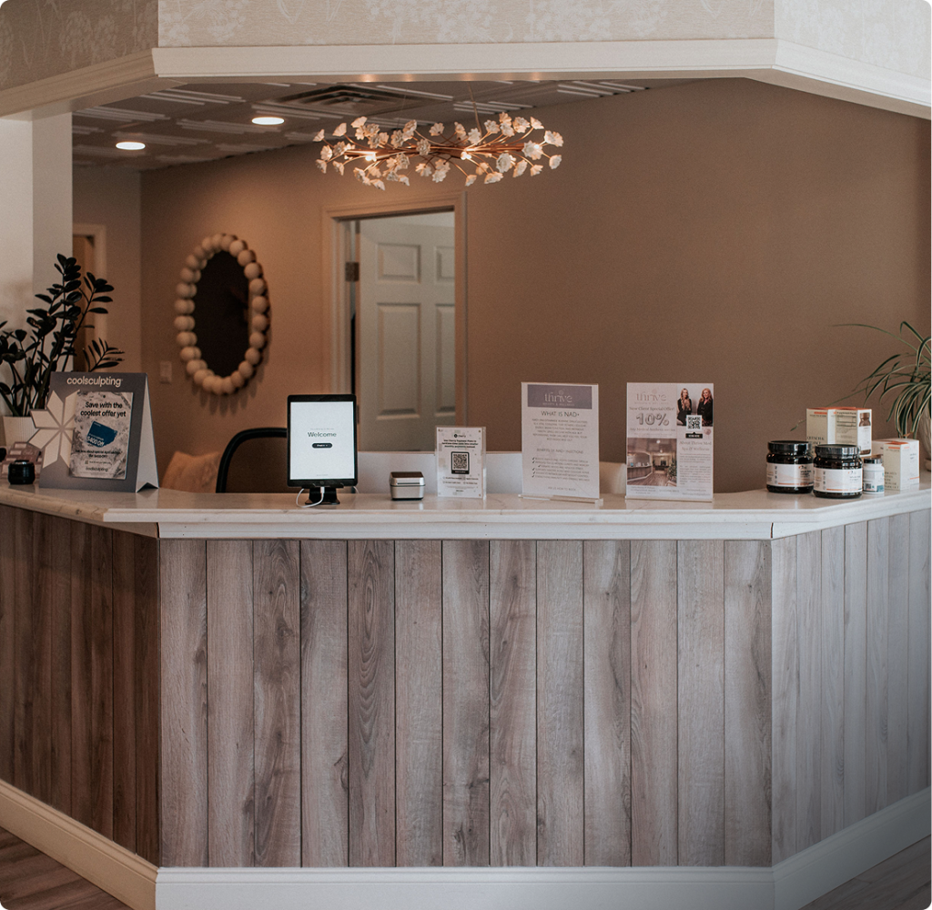 Thrive Med Spa & Wellness reception desk with welcome tablet, product displays, and decorative gold leaf pendant light
