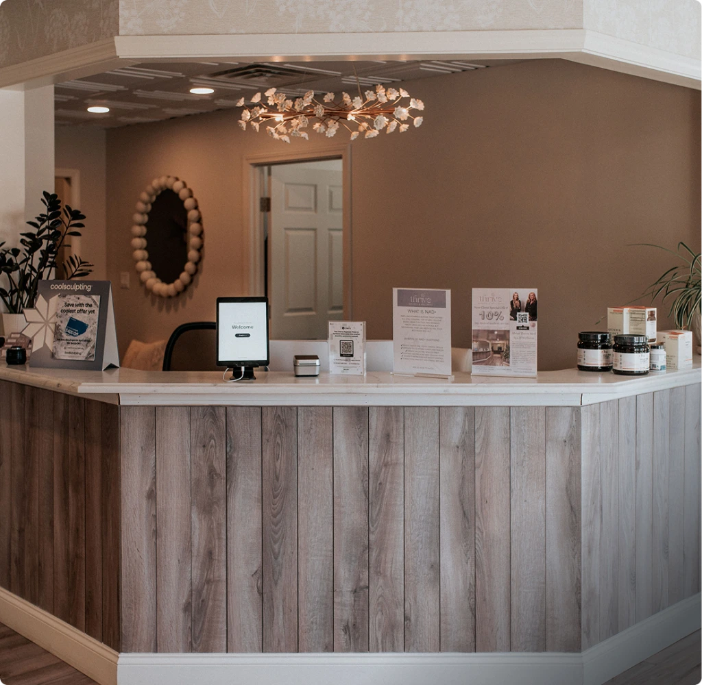 Thrive Med Spa & Wellness reception desk with welcome tablet, product displays, and decorative gold leaf pendant light