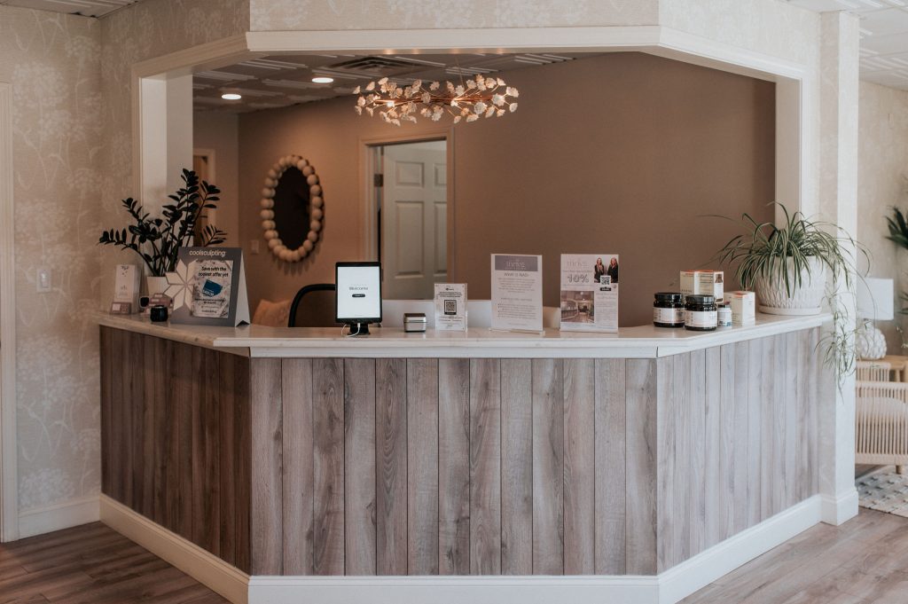 Thrive Med Spa + Wellness reception desk with warm tan walls, wooden paneling, copper mirror, and skincare products on display