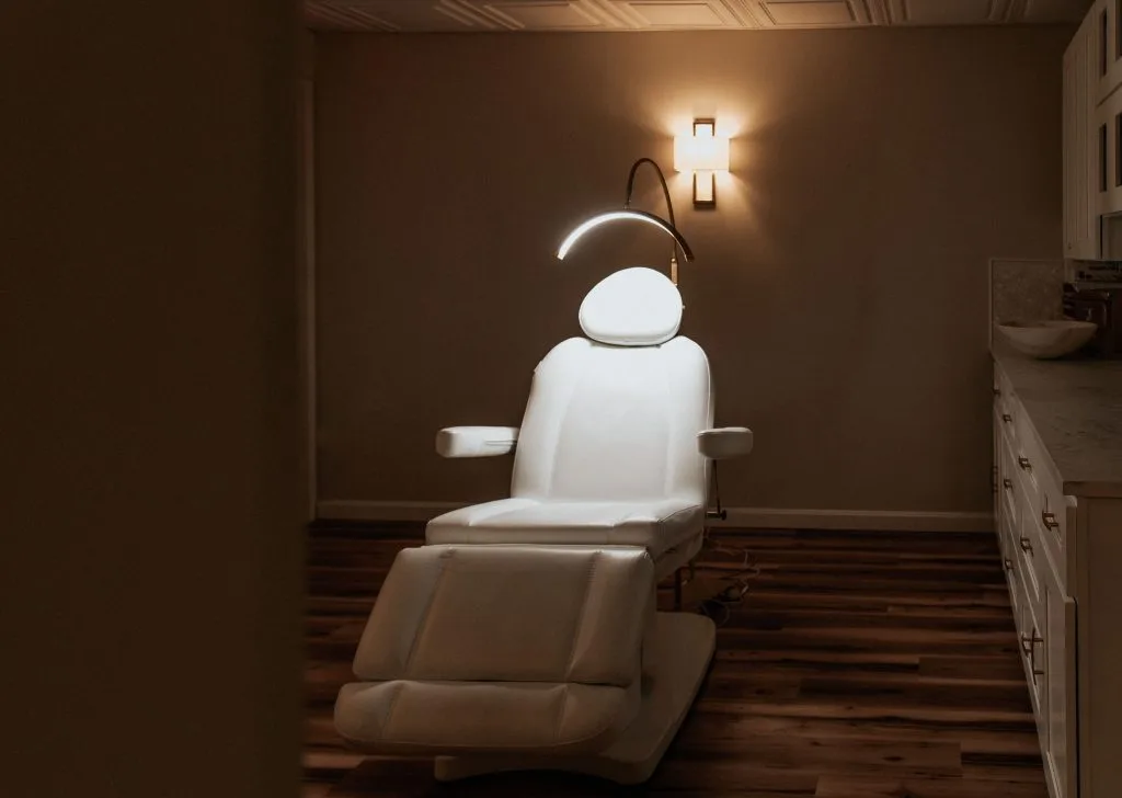 Modern treatment chair with overhead lamp in a warm-lit clinical room at Thrive Med Spa + Wellness