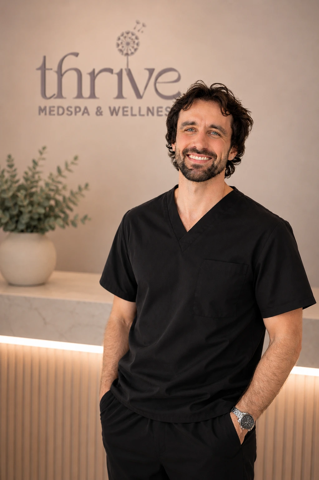 Tom Barrow, massage therapist at Thrive Med Spa & Wellness, smiling in front of the practice logo