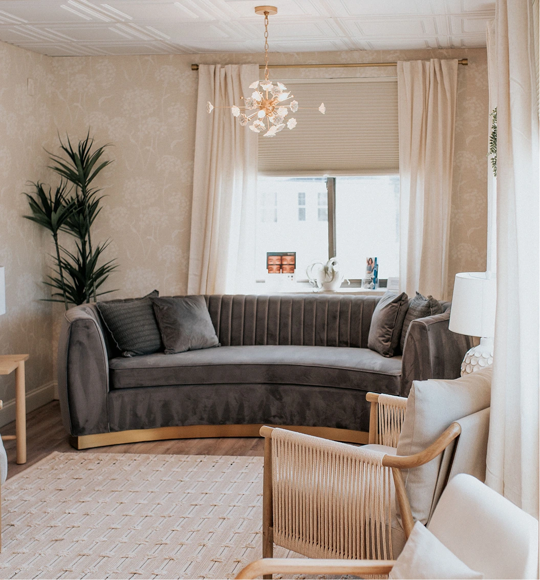 Thrive Med Spa + Wellness Portsmouth waiting room with curved gray sofa, wooden chairs, pendant lighting, and plant décor