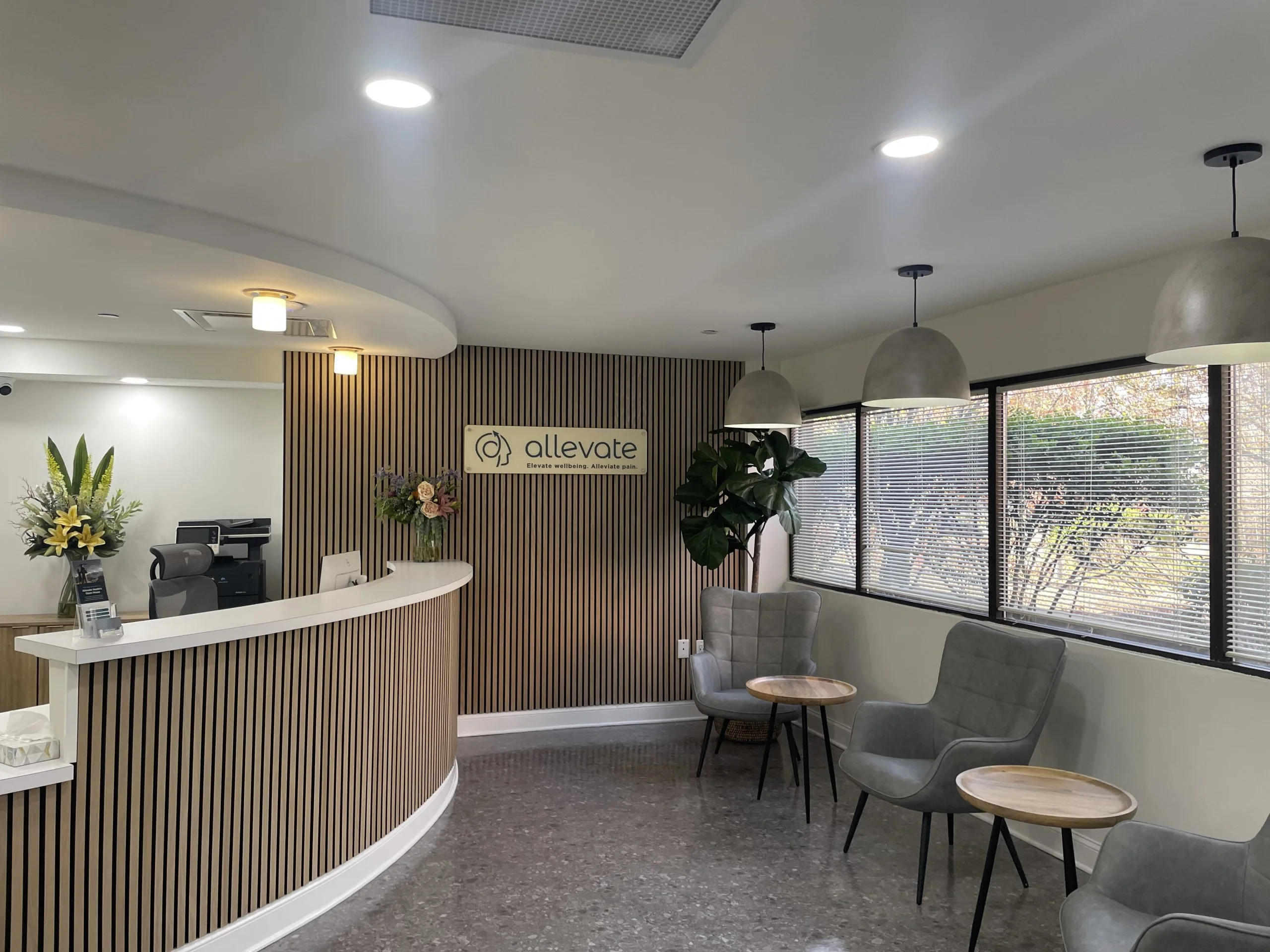 Allevate Health reception area with curved front desk, wood-slat accent wall, logo signage, waiting seating, and potted plants