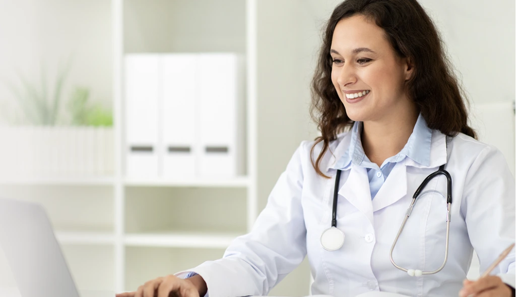 Healthcare provider in white coat with stethoscope smiling at patient during clinical consultation