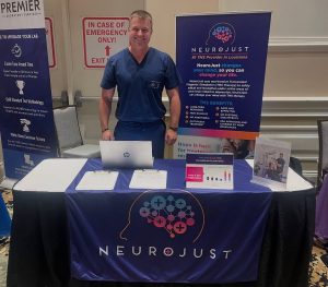 Provider standing at Neurojust booth displaying TMS therapy information and equipment at medical event