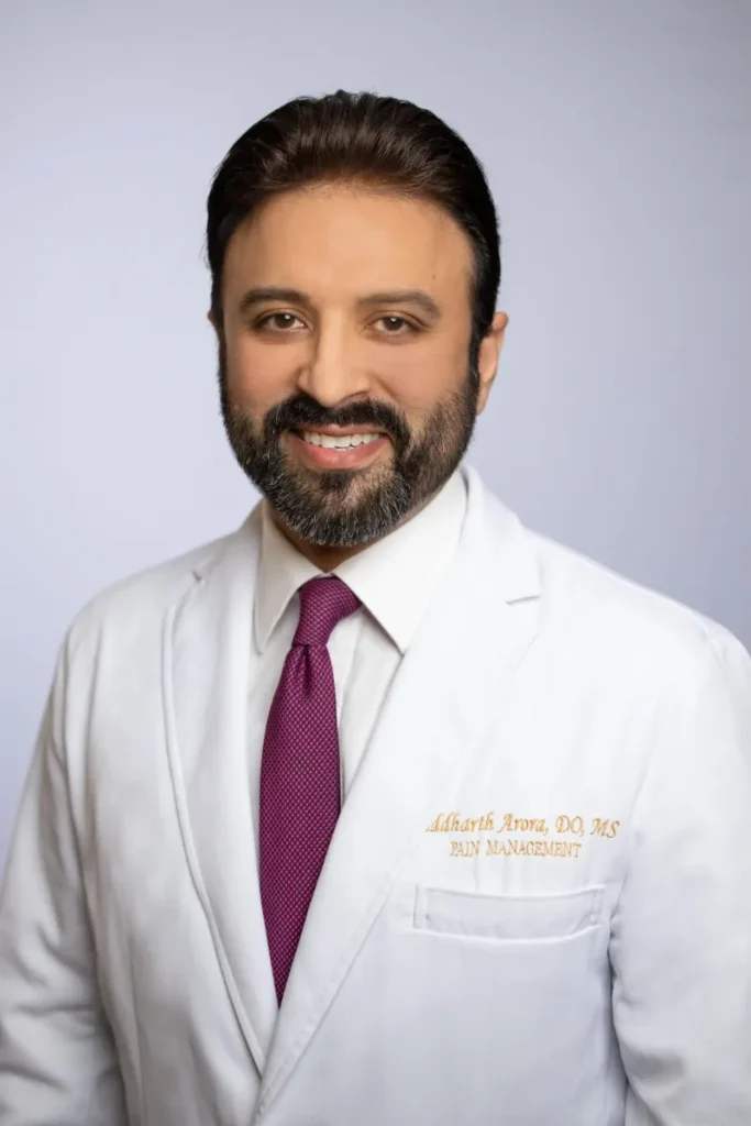 Siddharth Arora, DO, MS, pain management specialist, in white coat and purple tie