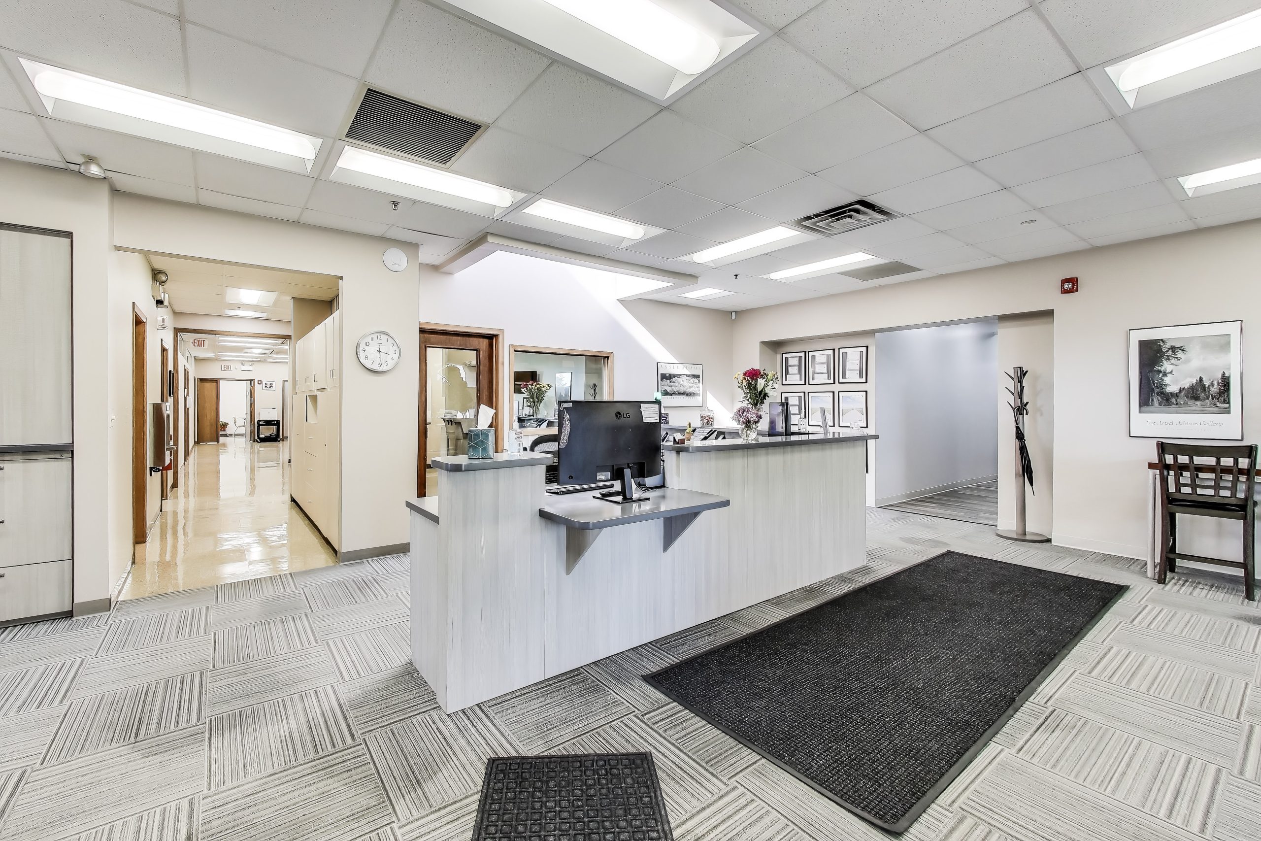 Reception desk with computer monitor in a bright clinical waiting room with artwork and doorways