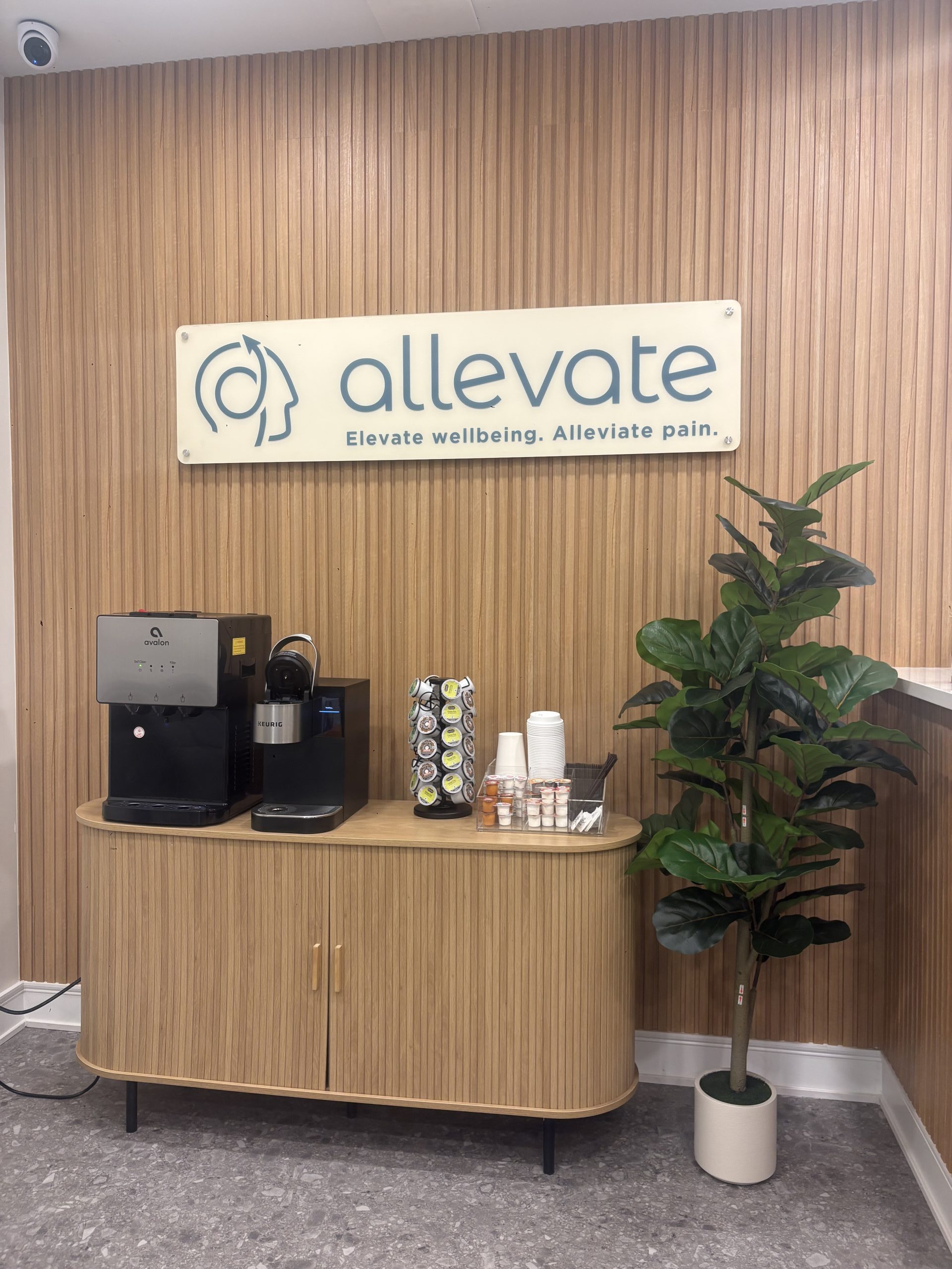 Allevate practice reception desk with logo sign, potted plant, water dispenser, and supplies