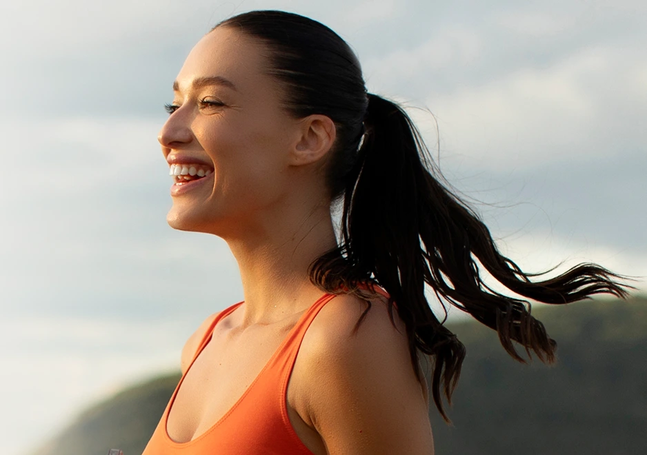 Woman smiling outdoors in bright daylight, symbolizing wellness and mental health improvement