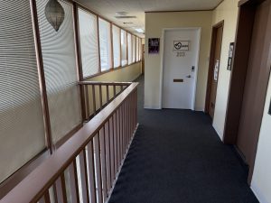 Hallway with frosted glass partitions, office door numbered 203, and dark carpeting in a medical office building