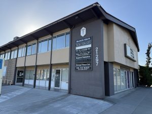 Modern medical office building exterior with large windows and directory sign listing multiple practices including Balanced Health and DeLago Primary Care