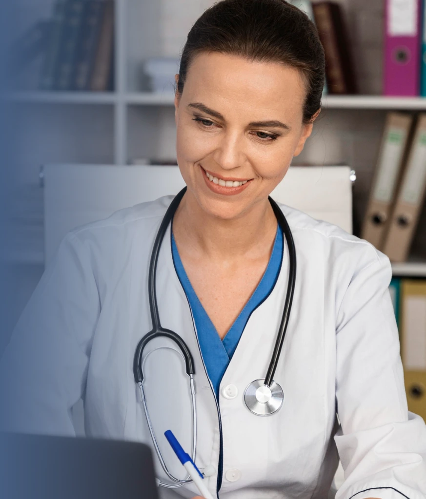 Healthcare provider in white coat with stethoscope reviewing information on laptop